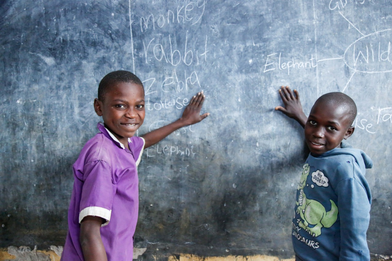 Two boys pointing at animal names on a chalkboard